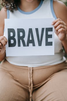 Close-up of a woman holding a sign saying 'Brave', emphasizing self-love and empowerment.