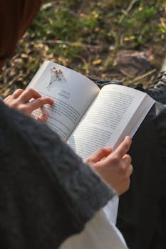 Person reading a book outdoors in a peaceful natural setting.