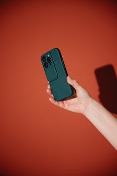 A hand holding a modern smartphone captured against a vibrant red backdrop.