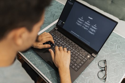 A man working on a laptop with AI software open on the screen, wearing eyeglasses.