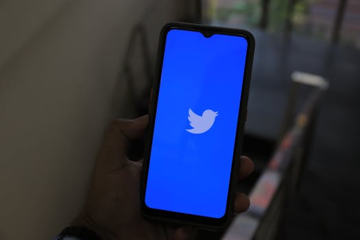 Close-up of a hand holding a smartphone displaying the Twitter app screen.