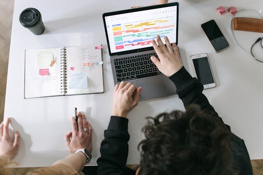 Two people collaborating on a laptop and planner at a vibrant modern office desk.